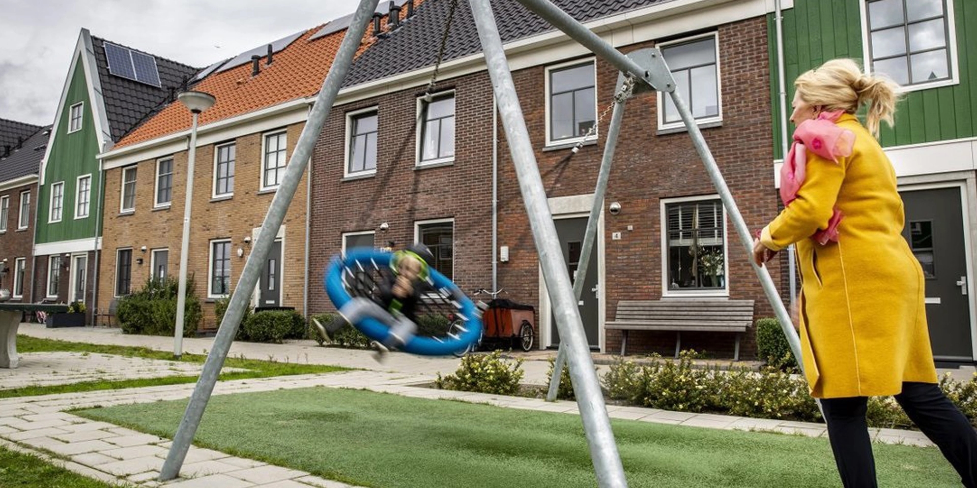 Vrouw duwt kind op schommel in een speeltuintje voor rijwoningen