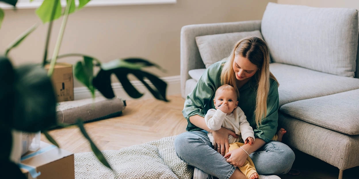 Vrouw zit met haar baby op de grond in de woonkamer