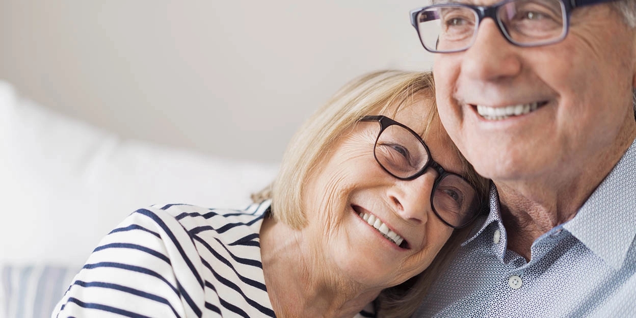 Ouder echtpaar zit lachend op de bank