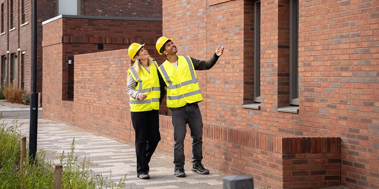 Man en vrouw kijken blij omhoog naar een nieuwbouwwoning