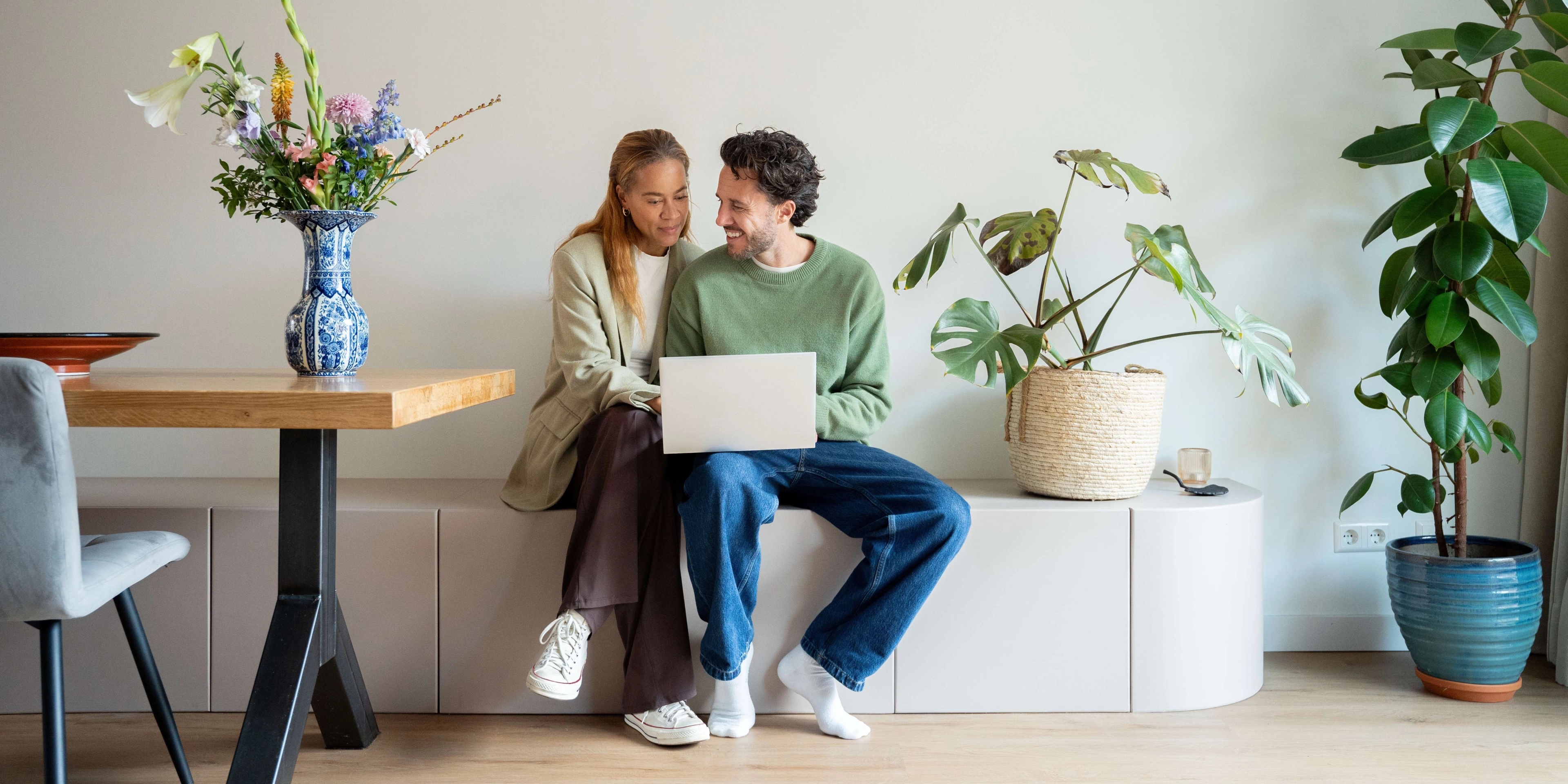 Jong stel zit lachend achter de laptop bij de eettafel